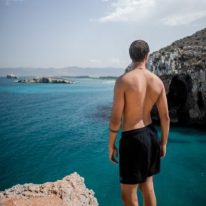 man in black shorts standing on rock formation near body of water during daytime